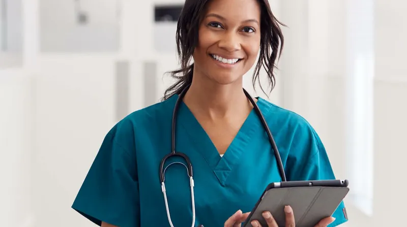 Pflegerin mit Tablet lächelt im Klinikflur