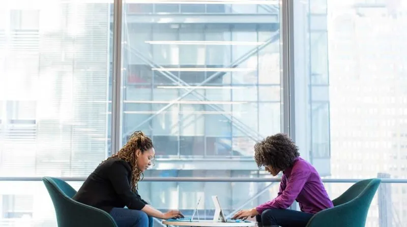 Zwei Frauen im Gespräch an einem Tisch mit Laptop